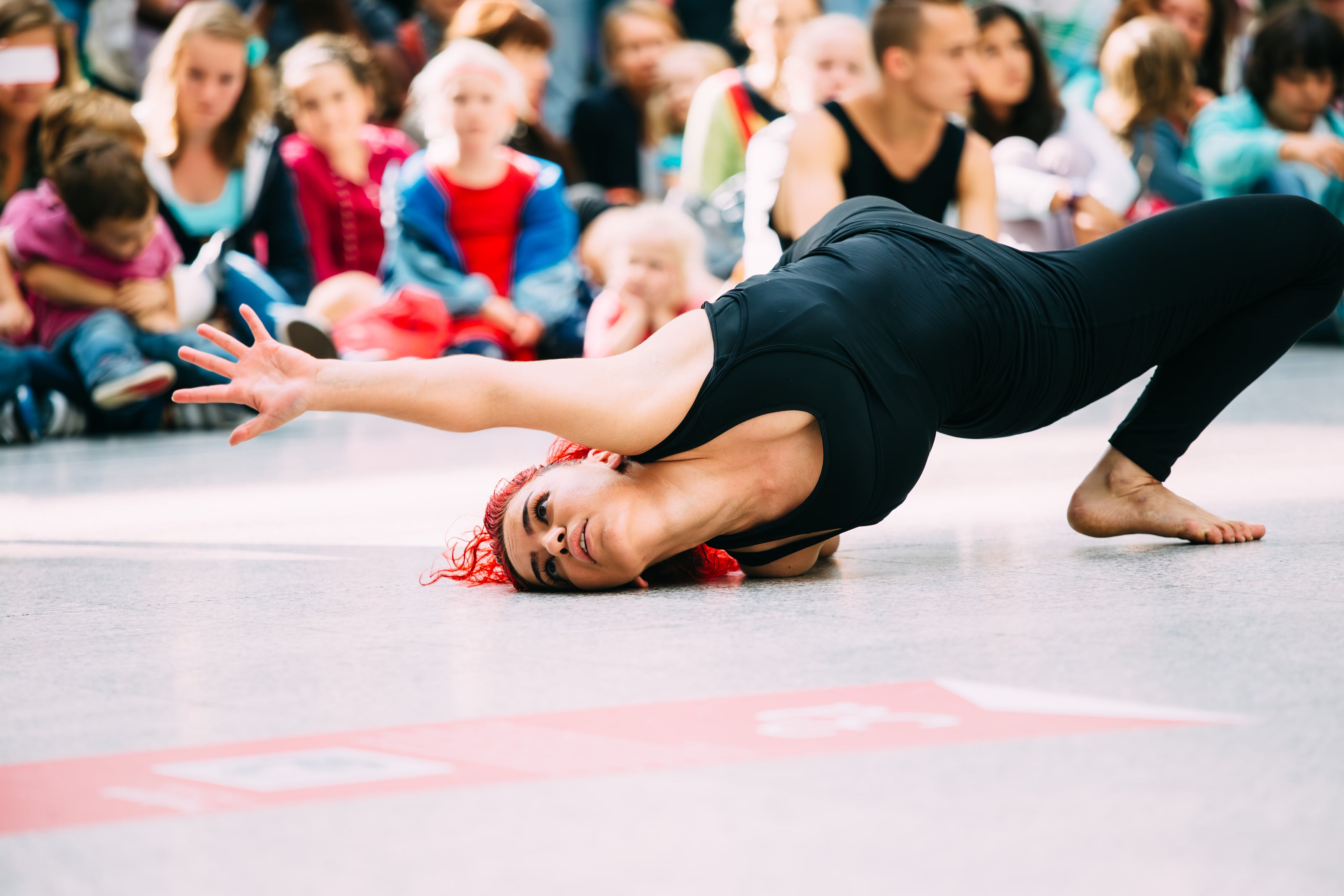Dancer lies low on the floor before a seated audience.