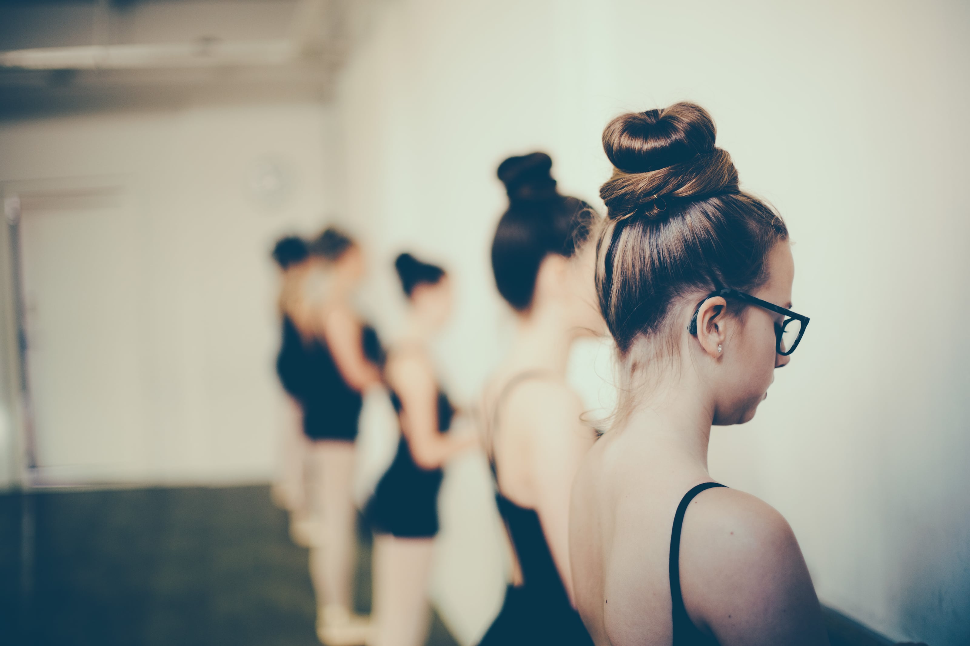 Dancers in black practice wear stand along a barre in a studio.