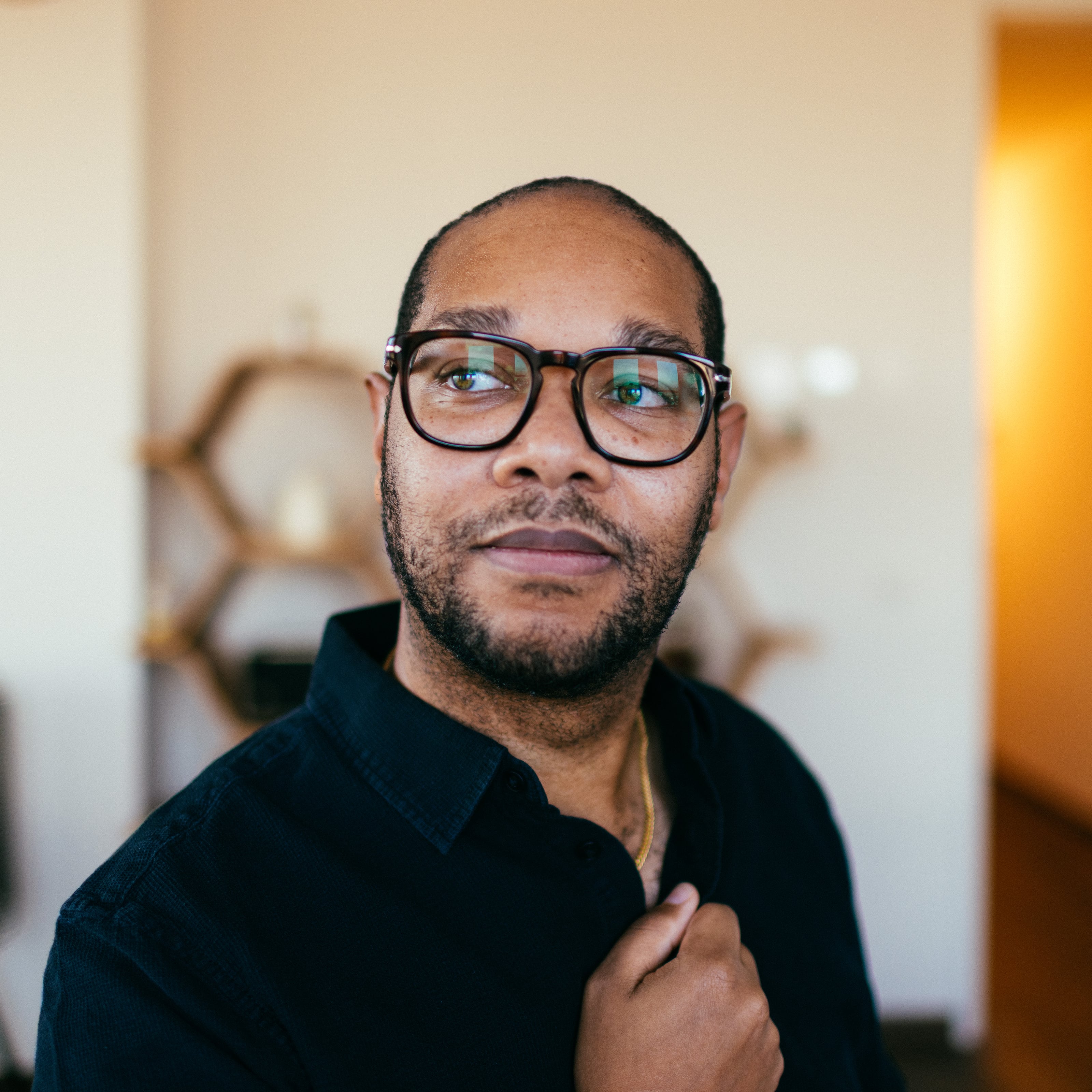 Person with glasses looks past the camera in a softly blurred room.