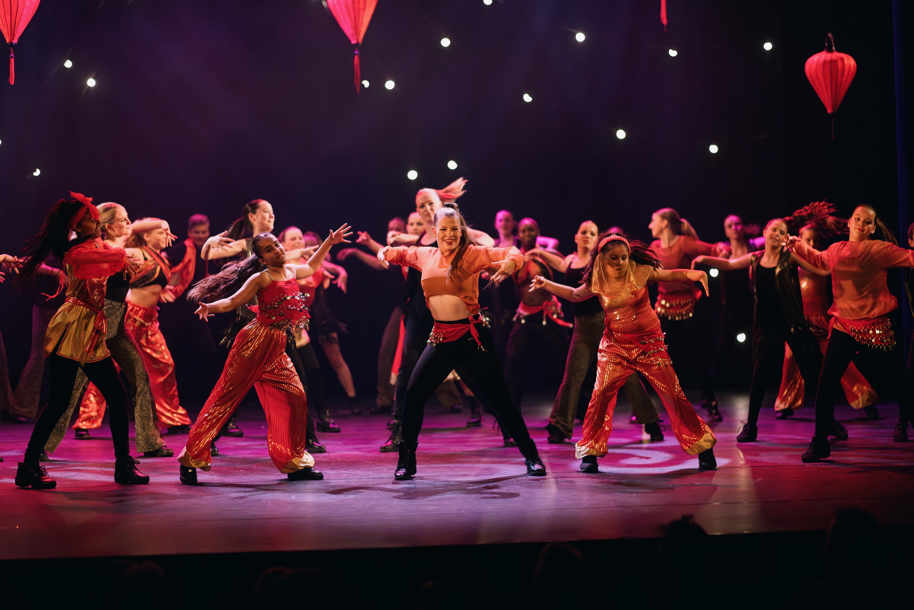 Groep dansers treedt op op een podium met rode lantaarns.